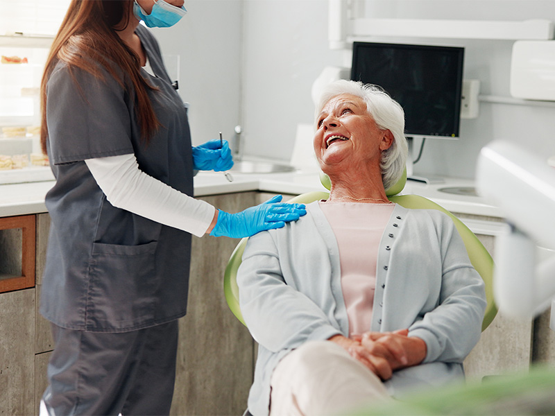 Ältere Frau beim Zahnarzt lächelnd im Beratungsgespräch über ästhetischen Zahnersatz in Lüdenscheid mit behandelnder Zahnärztin und Prüfung der Mundgesundheit.