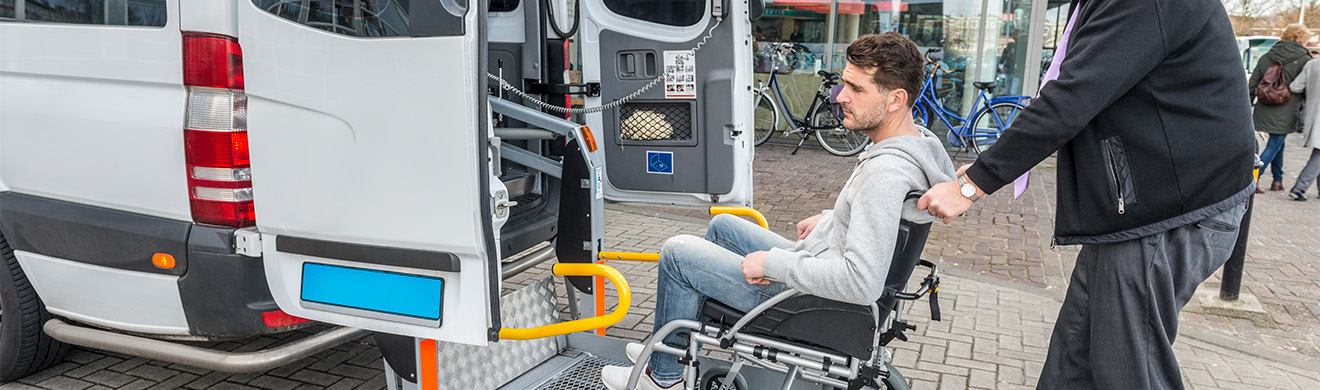 Fahrdienstmitarbeiter hilft Rollstuhlfahrer beim sicheren Einstieg in ein barrierefreies Fahrzeug für einen komfortablen Fahrdienst mit Rollstuhl.