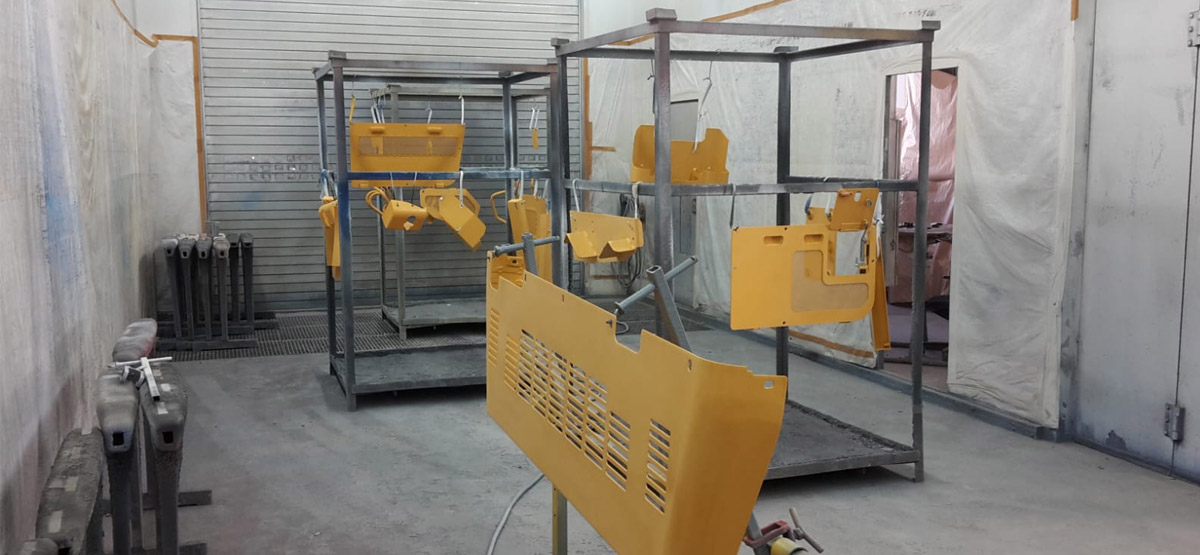 Gelb lackierte Maschinenbauteile stehen auf Gestellen in einer Lackierkabine von Benfer & Schneider in Wenden.