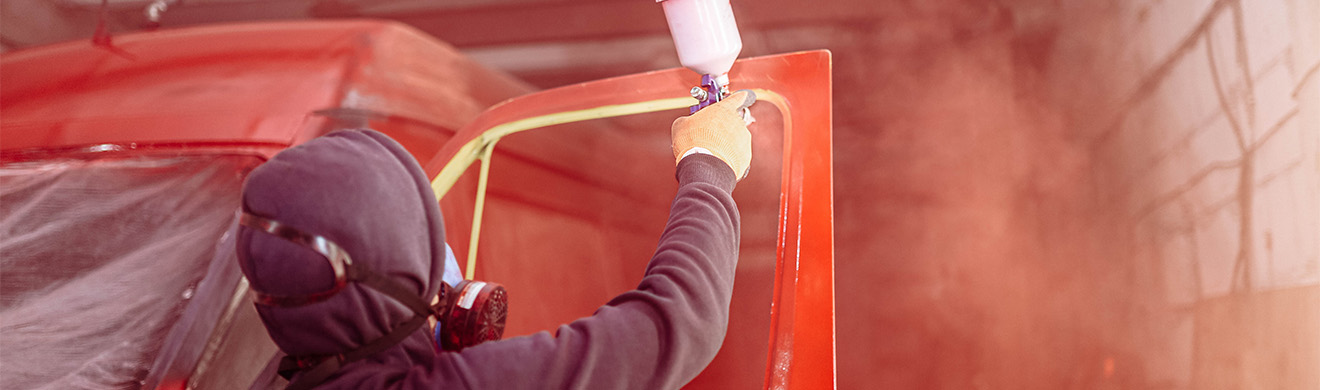 Roter Lkw wird in einer Werkstatt mit Spritzpistole lackiert – Beispiel für Industrie- und LKW-Lackierung in Freudenberg.