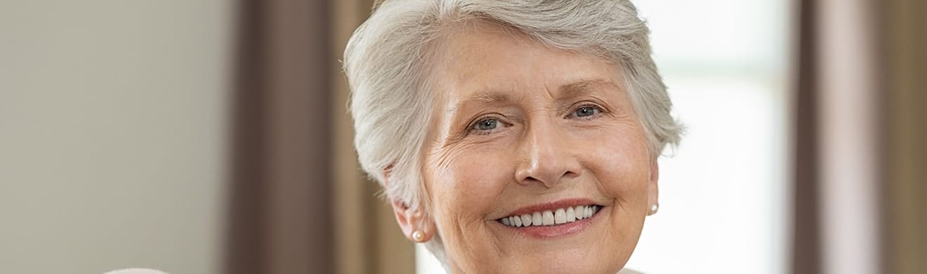 Seniorin zeigt strahlendes Lächeln nach Keramikkronen in Lüdenscheid, gesund und ästhetisch wirkender Zahnersatz.