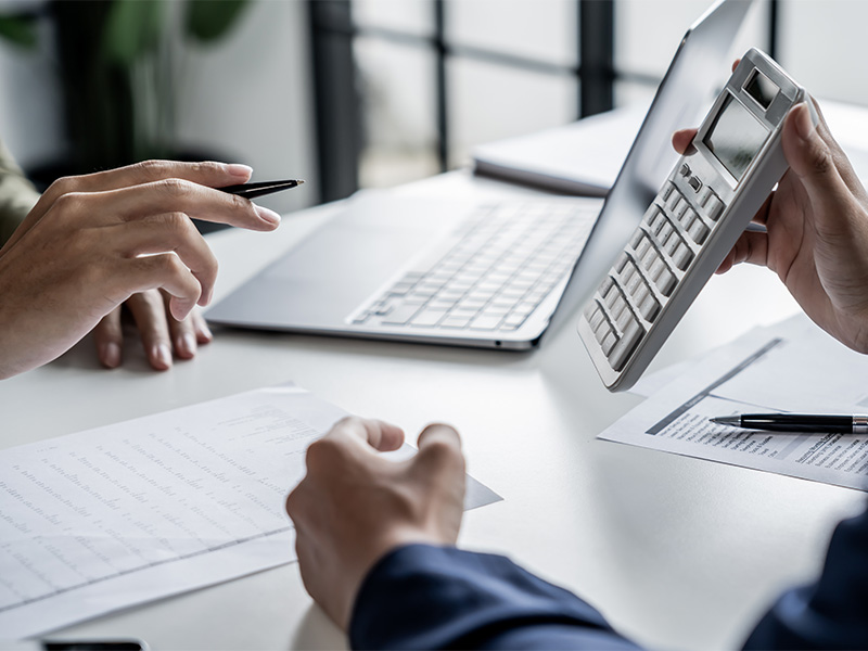 Fachfrau arbeitet am Rechner und Steuerberater mit Taschenrechner an Buchhaltungsunterlagen, symbolisiert professionelle Jahresabschlussprüfung in Lüdenscheid für Unternehmen.